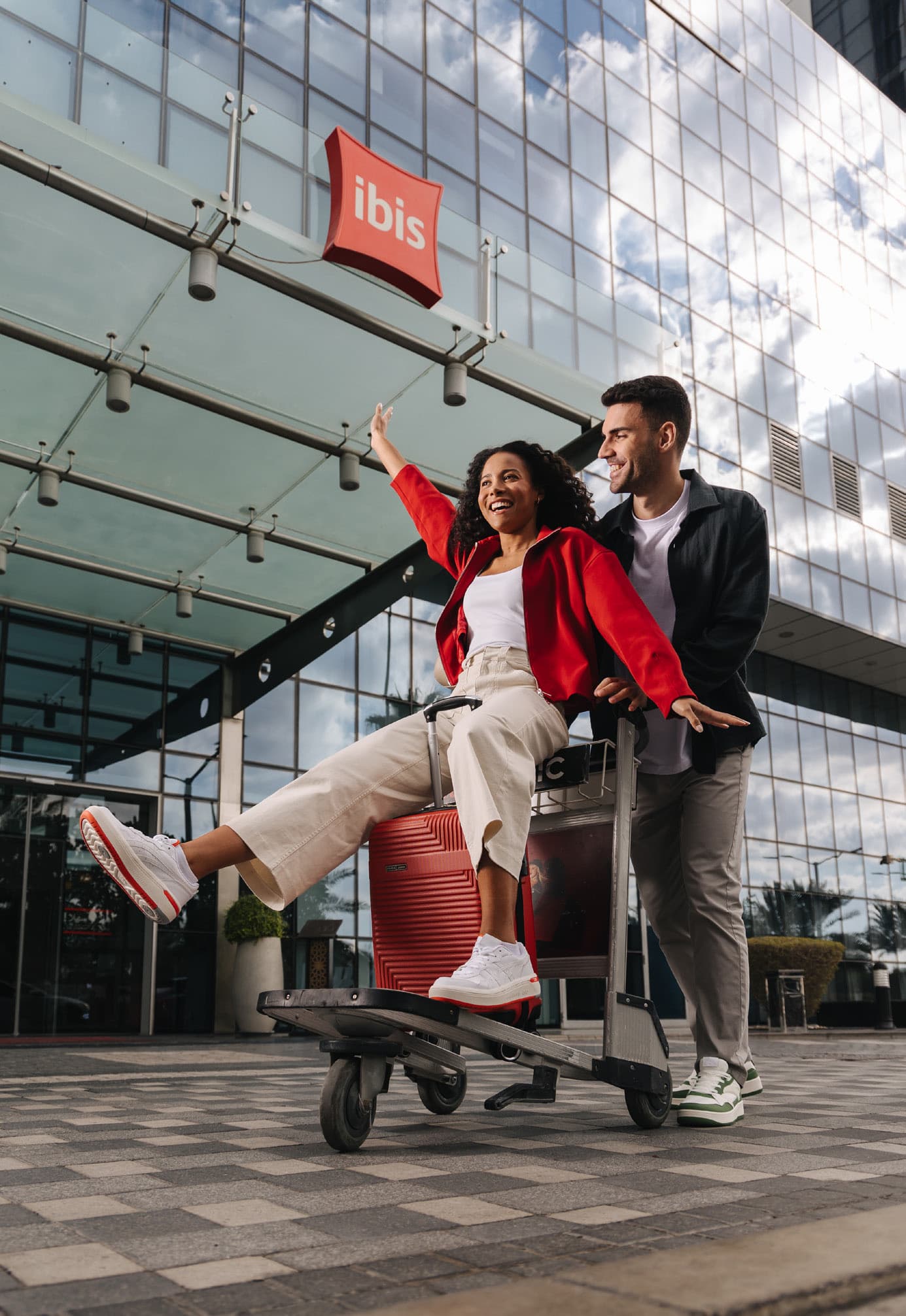Couple playing on a luggage trolley outside an Ibis hotel