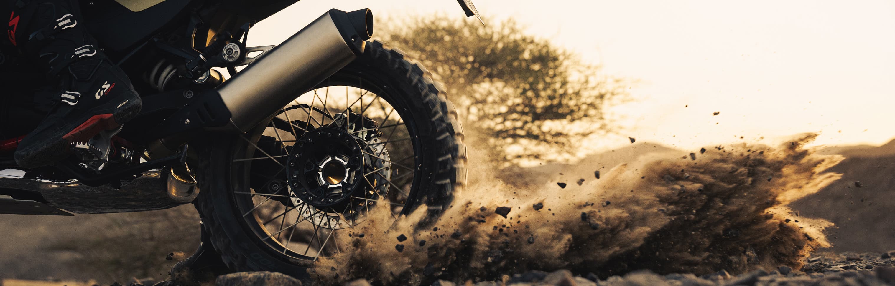 BMW enduro rear wheel tearing through dirt at golden hour